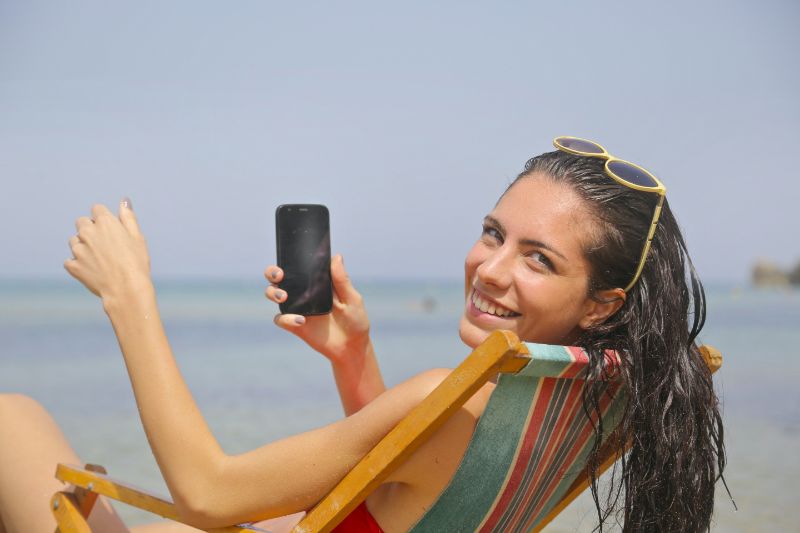 Ein hübsches Mädchen sitzt mit Handy im Liegestuhl am Strand.